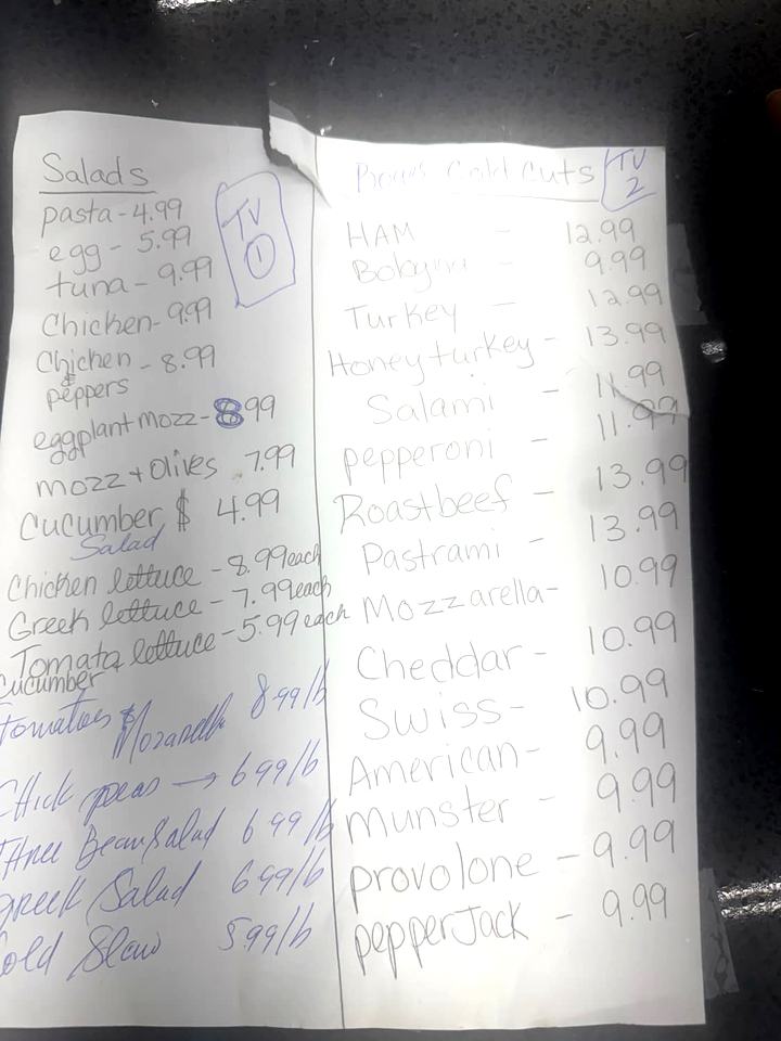The handwritten price board posted at the Geronimo's Deli counter, listing salads and Boar's Head cold cuts.